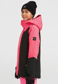 Kleurrijke skijas in roze en zwart met een capuchon, voorzien van een logo op de borst en een ritszak aan de zijkant. Een paar zwarte handschoenen.