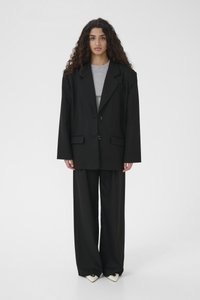 Must suurpärane jakk kahe nupuga, kombineeritud halli tihedalt istuva topi ja laiade mustade pükstega. Tekstuuriga kangas siledaga viimistlusega.