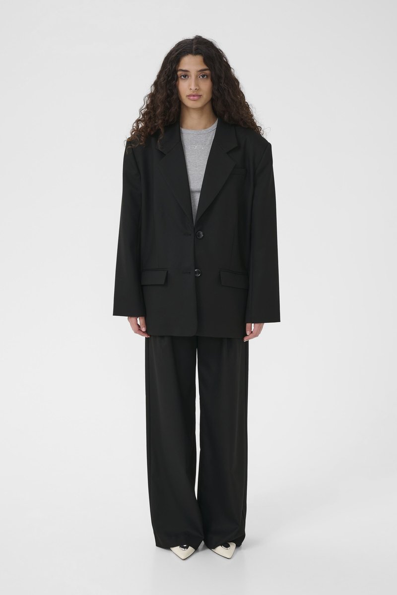 Svart oversize-kavaj med två knappar, kombinerad med grå figurnära topp och svarta byxor med vida ben. Texturerat tyg med slät yta.