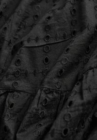 Tissu noir avec un motif œillet brodé présentant des formes circulaires et ovales disposées en grille.
