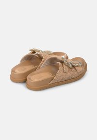 Sandales à glissière beiges avec un motif floral texturé, de grands nœuds décoratifs et une semelle en caoutchouc pour une bonne adhérence et durabilité.