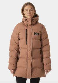 Chaqueta tipo puffer marrón con un alto cuello, bolsillos con cremallera y un logo negro. Presenta un diseño acolchado y una silueta ligeramente entallada.