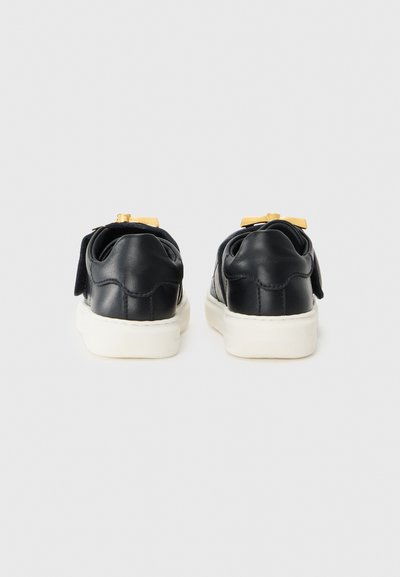 Svarta lädersneakers med en vit gummisula, med en rosettdekoration på hälen och en strukturerad detalj på bakpanelen.
