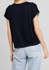 Marinblå kortärmad topp med lös passform, rund hals och subtil detalj på sidan. Matchad med ljusblå denimbyxor. Slät textur.