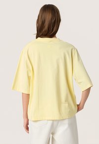 Tricou din bumbac galben, cu o croială lejeră, mâneci scurte și guler rotund. Presează un logo subtil embosat pe spate.