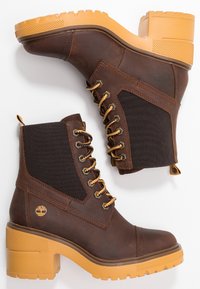 Paire de bottines en cuir marron avec semelles épaisses jaunes, lacets à l'avant et panneaux élastiques sur les côtés, présentées sur fond blanc.