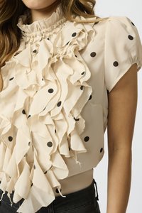Beige paita, jossa on mustat pilkut, rypistetty etuosa ja korkea, frillattua kaula-aukko. Lyhyet hihat elastisilla yksityiskohdilla.