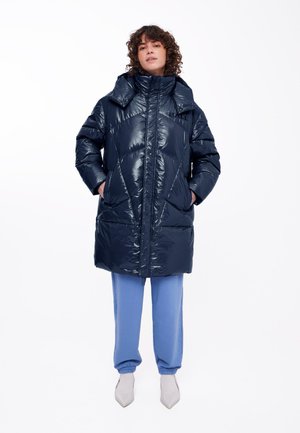 Navy puffer coat with a glossy finish, featuring a high collar, diagonal stitching, and two side pockets. Paired with blue pants.