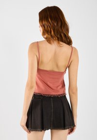 Ribbete rose tanktopp med tynne stropper, sammen med et svart plisségalleri laget av denim med en frynsete kant. Glatt tekstur og tettsittende design.
