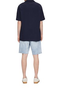 Marineblauw T-shirt met korte mouwen en een relaxte pasvorm, gecombineerd met lichtblauwe denimshorts. Witte sneakers met een lichtbruine zool maken de outfit compleet.