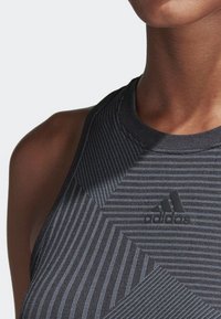 Top deportivo negro sin mangas con rayas texturizadas y cuello alto. Incluye un logo elevado en negro de "adidas" en la parte frontal.