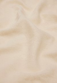 Asciugamano in cotone beige con superficie testurizzata, mostrato in morbide pieghe. Il materiale appare morbido e assorbente, senza motivi o accenti distintivi.