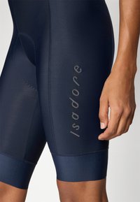 Marineblå sykkelshorts med glatt tekstur, med høy midje og reflekterende logo-detaljer langs siden.