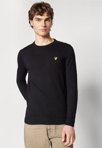 Maglione nero lavorato a maglia con collo rotondo, maniche lunghe e orlo a coste. Presenta un piccolo logo di un'aquila gialla sul petto.