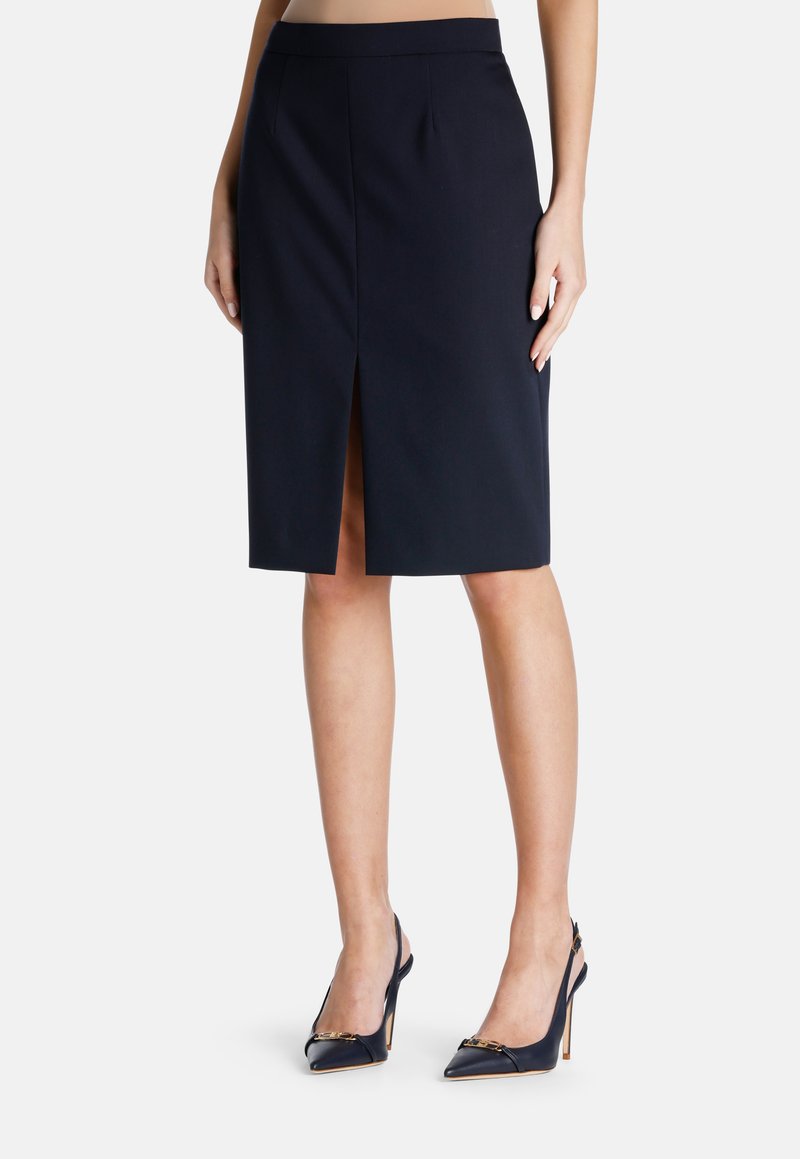 Marinefarbener Bleistiftrock mit Schlitz vorne, taillierter Schnitt und glatter Textur. Kombiniert mit marineblauen Slingback-Pumps mit goldenen Akzenten.