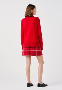 Czerwony sweter z dzianiny z wysokim kołnierzem, w zestawieniu z mini spódnicą w czerwono-czarną kratę. Czarny płaski obuwie dopełnia strój.