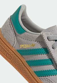 Baskets en suède gris avec des accents turquoise, logo "SPEZIAL" doré, semelle en gomme texturée et trois rayures crantées sur le côté.