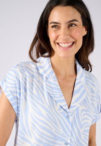 Camicia azzurra chiara a maniche corte con strisce bianche a zebra, design con colletto e due bottoni sul davanti. Tessuto morbido.