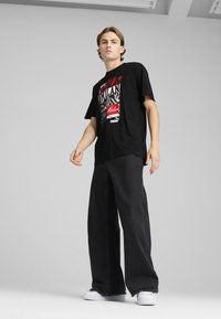 Sort grafisk t-shirt med rød og hvid print med "Milan" på forsiden, parret med vidde ben sorte jeans og hvide sneakers.