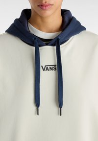 Felpa beige con cappuccio blu navy, con lacci azzurri e un logo "VANS" nero sul davanti. Texture liscia e design casual.