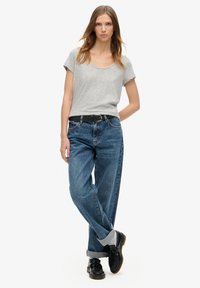 T-shirt gris à manches courtes associé à un jean bleu taille haute, avec une ceinture noire. Le mannequin porte des chaussures noires avec des semelles épaisses visibles.