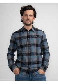Camisa de cuadros en tonos azul, gris y negro. Tela suave con botones y dos bolsillos en el pecho. Mangas largas con puños abotonados.