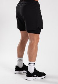 Shorts de sport noirs avec une couche intérieure, fabriqués à partir d'un matériau doux. Assortis avec des baskets noires et des chaussettes blanches à rayures noires.