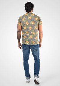 Hérres kortærmet skjorte i grå med et blomsterdesign i orange og grøn. Kombineret med blå denim jeans og hvide sneakers.