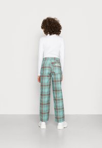 Calças xadrez em turquesa e castanho com um corte solto, apresentando dois bolsos traseiros e uma marca bordada no bolso direito.