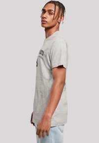 Grau Baumwoll-T-Shirt mit kurzen Ärmeln, mit schwarzem Drucktext und Grafik auf der Vorderseite, lockere Passform und glatte Textur.