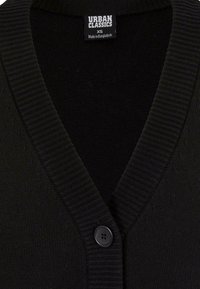 Cárdigan negro de punto con cuello en V, cuello acanalado y cierre con un solo botón. La etiqueta dice "URBAN CLASSICS", talla XS, hecho en Bangladesh.