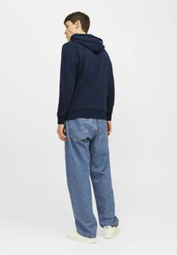 Marine blauwe hoodie met een trekkoordcapuchon, gecombineerd met losse, lichtblauwe denim jeans. Witte sneakers maken de outfit af.