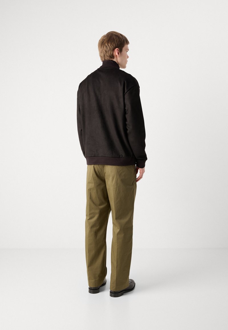 Schwarzes Sweatshirt mit geripptem Kragen und Bündchen, kombiniert mit olivgrünen, lockeren Hosen. Glatte Texturen mit minimalen Details.