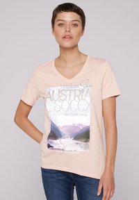 Jasnoróżowa bawełniana koszulka z dekoltem w serek, z nadrukowanym wzorem górskiego krajobrazu oraz tekstem: "Austria" i "Odpocznij. Odśwież się. Odnów."