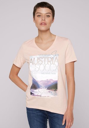 Camiseta de algodón de color rosa claro con escote en V, que presenta un diseño impreso de un paisaje montañoso y el texto: "Austria" y "Descansar. Refrescar. Renovar."