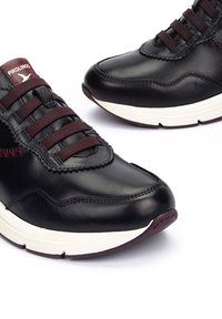 Baskets en cuir noir avec des lacets épais bordeaux, des semelles intermédiaires blanches et des accents rouges. Présentent des détails cousus et une forme de bout arrondi.
