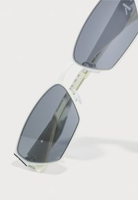 Sunscreenbriller med hvit plastramme, gråtonede linser, vinkelrett form og klare nesepader; inkluderer metalliske detaljer for hengslene.