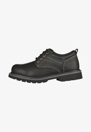 Scarpa da lavoro in pelle nera con punta arrotondata, cuciture beige e suola in gomma robusta. Progettata con chiusura con lacci e dettagli laterali.