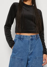 Svart, strukturerad långärmad crop top med rund halsringning, som matchas med lösa, ljusblå, högmidjade jeans med stora fickor.