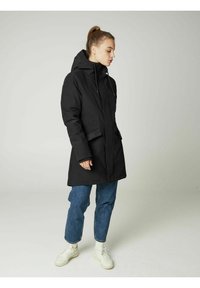 Juodas vandeniui atsparus parka su užtrauktuku priekyje, kapišonu ir dviem šoninėmis kišenėmis. Turintis tiesų kirpimą ir susitraukusius rankogalius; derinamas su džinsais ir sportbačiais.