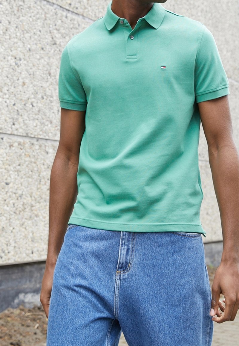 Green cotton polo shirt with a collared neckline and short sleeves, featuring a small logo. Paired with light blue denim jeans.