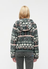 Fleeceová kapucňová bunda so vzorovaným dizajnom v odtieňoch teal, ružovej a smotanovej. Obsahuje manžety na rukávoch a lem, s mäkkým, texturovaným povrchom.