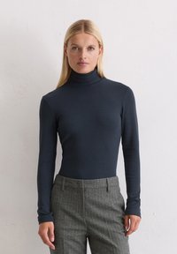 Donkerblauwe langemouwen coltrui gemaakt van rekbaar materiaal, gecombineerd met grijze gepinde streep tailored broek. Soepele textuur en aansluitend ontwerp.