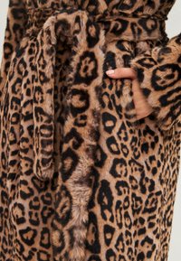 Bata de pel faux con estampado de leopardo y una textura suave, que incluye un cinturón y bolsillos laterales. Los colores son tonalidades de marrón y negro.