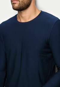 Granatowa koszula z długim rękawem wykonana z miękkiego materiału, z okrągłym dekoltem i dopasowanym krojem oraz subtelną teksturą. Minimalistyczny design bez wzorów.