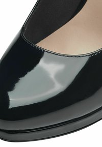 Chaussure à talon haut en cuir verni noir avec un bout arrondi et une finition lisse et brillante. L'intérieur est beige avec une texture douce. Détail de couture subtil.