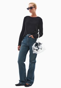 Czarna bluzka z długim rękawem, niebieskie dżinsy z wysokim stanem, czarne buty i pognieciona srebrna torebka. Modelka nosi ciemne okulary przeciwsłoneczne.