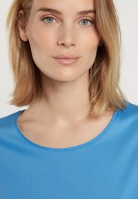Blauw scoop-neck top gemaakt van gladde stof, met een ronde halslijn en een eenvoudig, strakke ontwerp. Huidskleur zichtbaar, geen afleidende patronen.