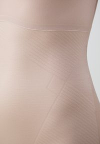 Nude seamless shapewear featuring a smooth texture, diagonal ribbed patterns, and a high waistband design providing gentle compression.