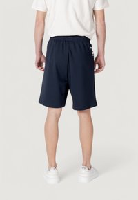 Shorts de sport bleu marine avec taille élastique, fabriqués dans un tissu léger, dotés de poches latérales et d'un accent de logo blanc.